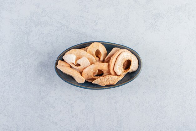 A black deep plate with healthy dried apples on stone background.