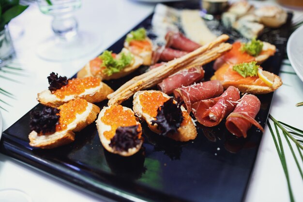 Black dish with snacks made of meat and caviar