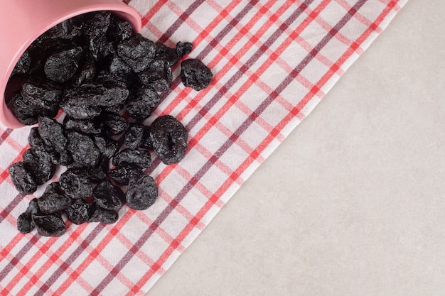 Black dry plums in a ceramic plate on concrete.