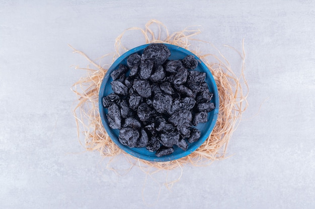 Free photo black dry plums in a cup on concrete surface