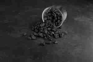 Free photo black dry sultanas out of a glass cup on black background.