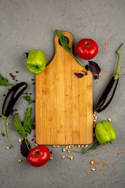 Black eggplants a top view of fresh ripe vegetables such as red tomatoes and green bell peppers along with green herbs and brown desk on a light floor