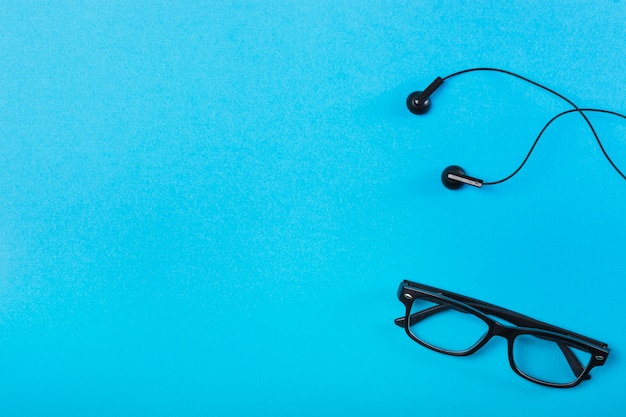 Black eyeglasses and earphone on blue background