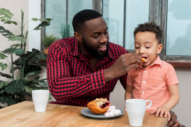 Black father feeding little son with croissant