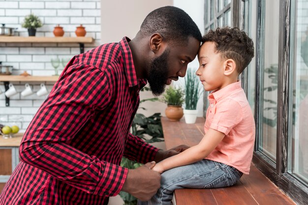 Black father holding hand of son on window sill