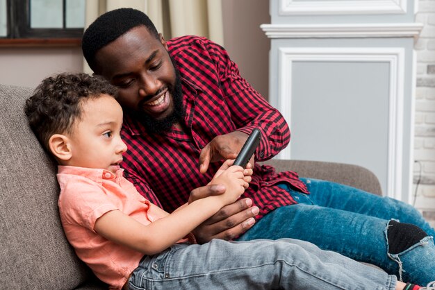 Black father and son using smartphone on couch