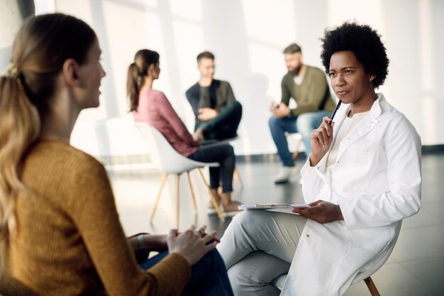 Black female doctor communicating with a woman during group psychotherapy meeting