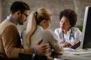 Free photo black female doctor showing to a couple their electronic medical record on touchpad while communicating with them at clinic