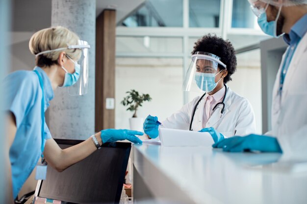 Black female doctor talking to a nurse while writing medical data at reception desk in the hospital