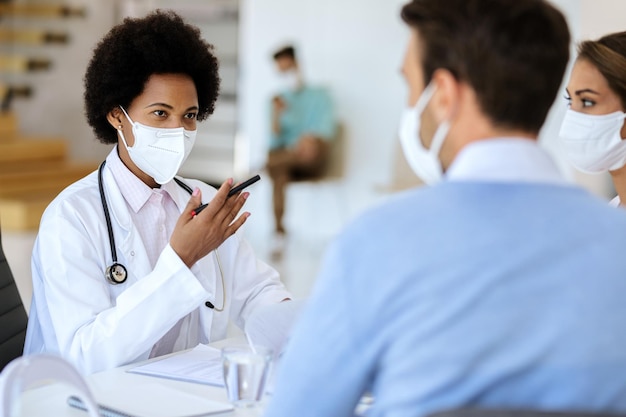 병원에서 부부와 이야기하는 동안 얼굴 마스크를 쓴 흑인 여성 의사