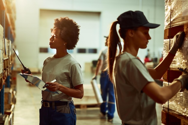 Free photo black female inspector with walkietalkie checking stock of products while working in a warehouse