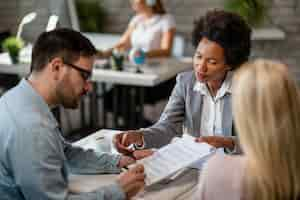 Free photo black female real estate agent showing to a couple where to sign the contract during the meeting in the office