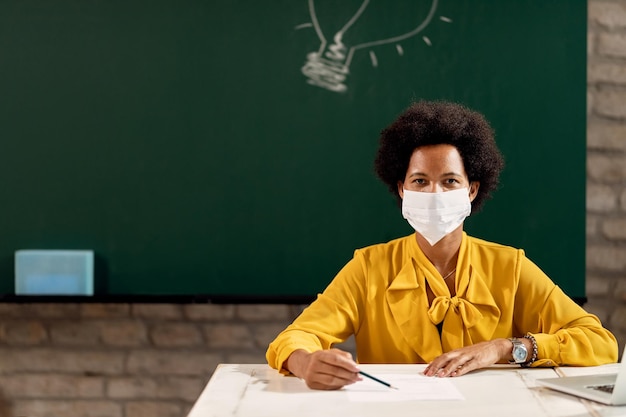 Free photo black female teacher wearing face mask while giving a lecture in the classroom