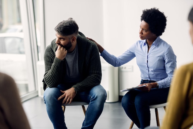 Black female therapist supporting a man who is talking abut his issues during group meeting