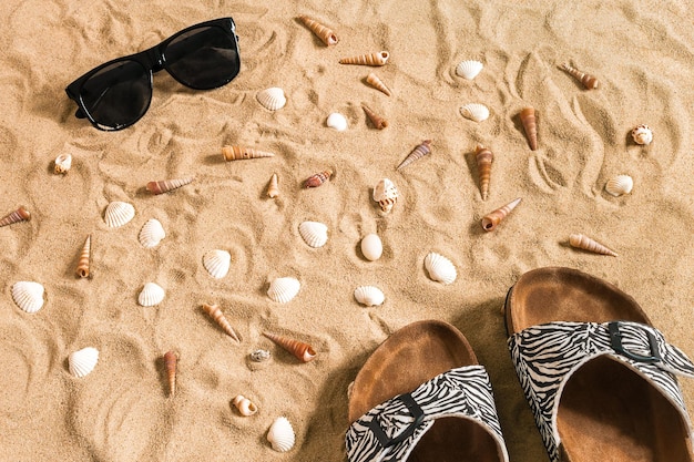 Free photo black flip-flops and sunglass, seashell on sand. with place for your text. top view. copy space. still life mockup flat lay