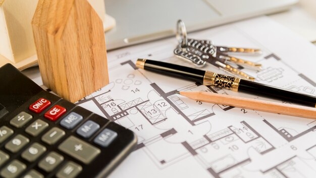 Black fountain pen; pencil; keys; wooden house block and calculator on blueprint