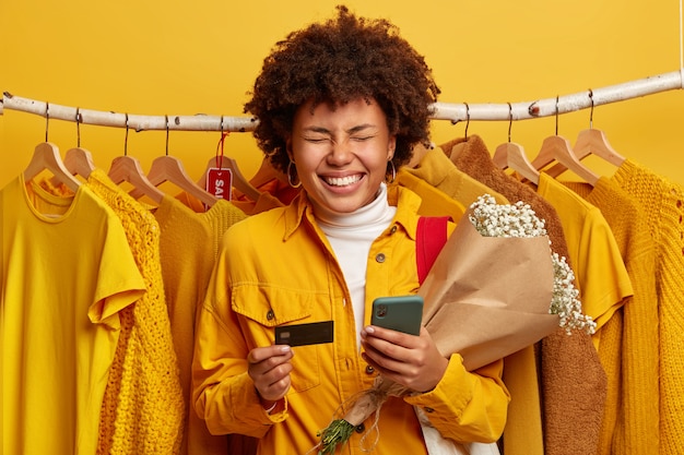 Black Friday and sales concept. Overjoyed dark skinned woman has curly hair, smiles broadly, holds bouquet