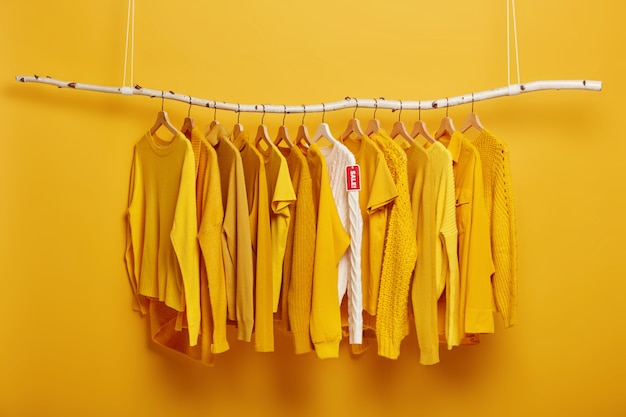 Black Friday, shopping and big sales concept. Detail image of yellow clothes and white sweater with label tag hanging on rack in clothing store.