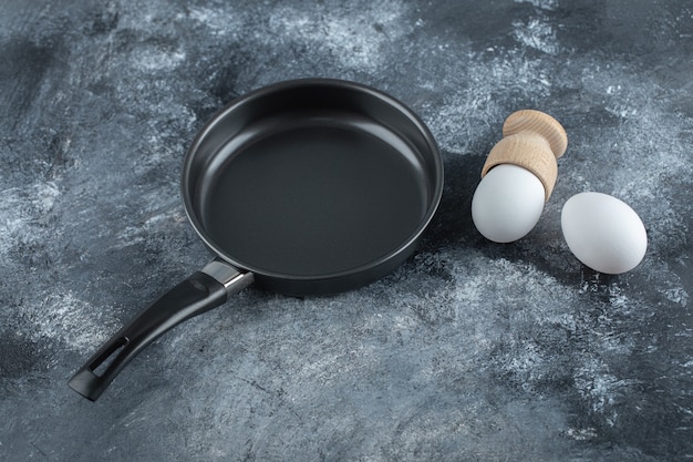 Black frying pan with two organic chicken egg on grey background