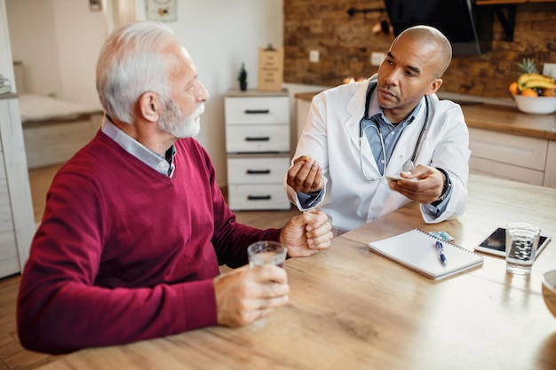 Free photo black general practitioner giving pill to a senior man during home visit