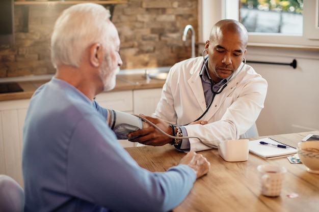 Black general practitioner measuring blood pressure of a senior man during home visit