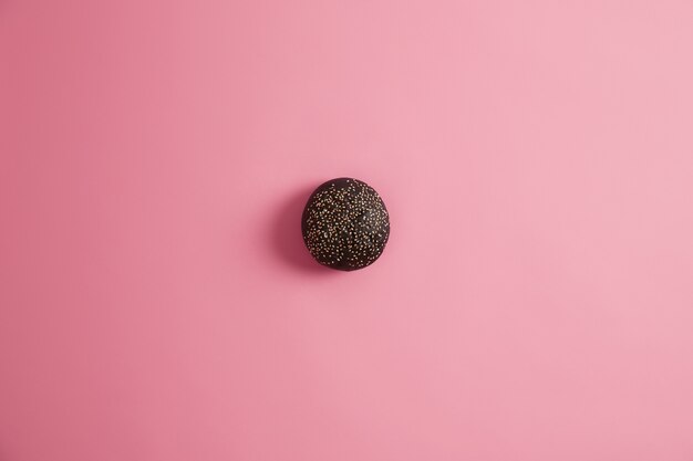 Black gourmet bread bun for making sandwich garnished with sesame seeds, isolated on pink  background. Junk food and unhealthy nutrition concept. Homemade burger. Delicious snack, fast food