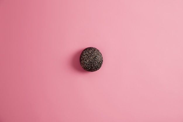 Black gourmet bread bun for making sandwich garnished with sesame seeds, isolated on pink  background. Junk food and unhealthy nutrition concept. Homemade burger. Delicious snack, fast food