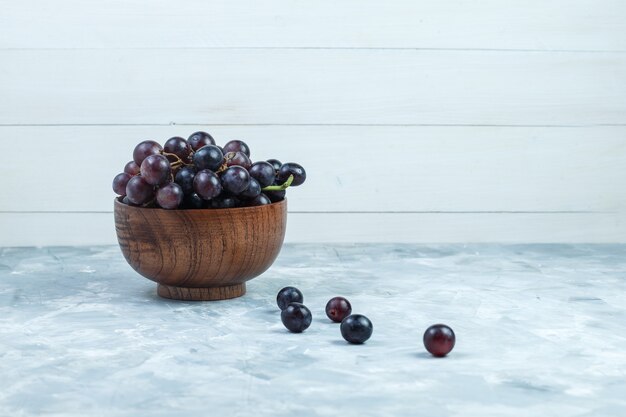 Black grapes in a clay bowl on grungy grey and wooden background. side view.