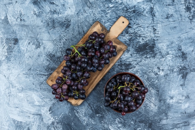 Free photo black grapes in a clay bowl on grungy plaster and cutting board background. flat lay.