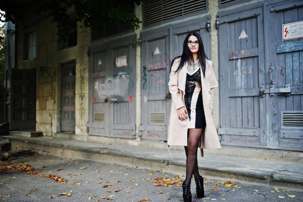 Black hair woman in glasses and coat posed on idustrial street