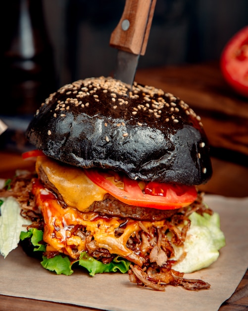 Черный гамбургер с ножом на столе