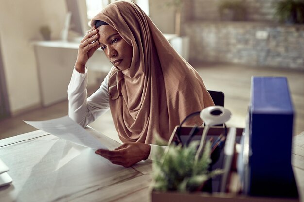 Black Islamic businesswoman feeling worried while going through paperwork in the office
