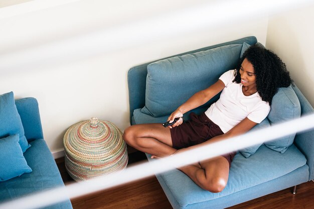 Black lady relaxing at home watching TV changing channel