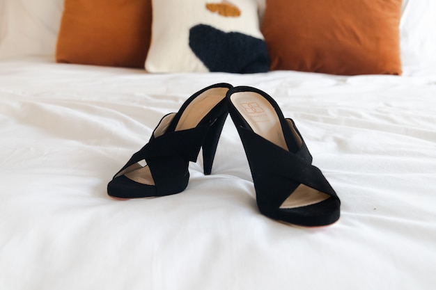 Free photo black leather peep-toe heeled sandals on white bed