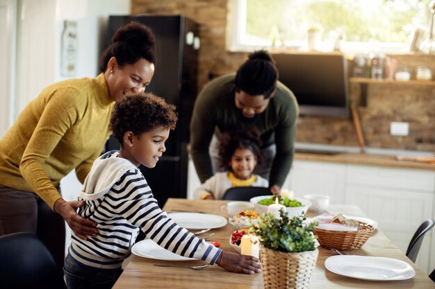 Черный маленький мальчик и его семья готовятся к обеду в столовой
