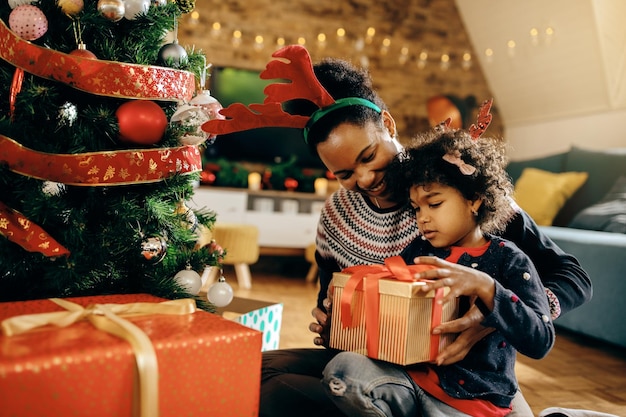 Bambina nera e sua madre che aprono i regali vicino all'albero di natale a casa