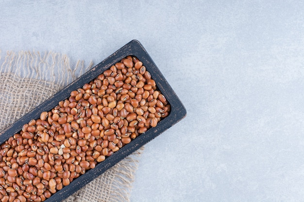 Black, long tray stocked with a mass of red beans on a piece of fabric on marble surface