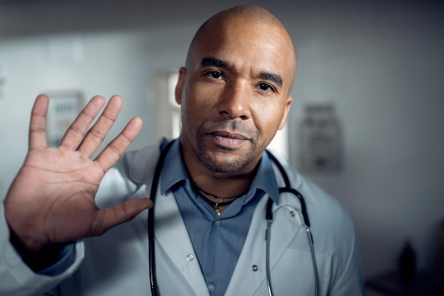Black male doctor waving during a conference call and looking at camera