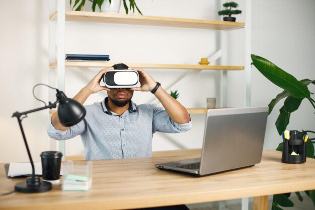 Черный предприниматель сидит в офисе и использует очки виртуальной реальности