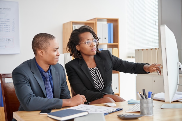 Black male and female colleagues sitting in office and looking at computer screen together