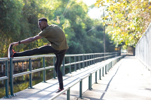 秋​の​朝​、​公園​の​道路​脇​で​ストレッチ​運動​を​している​黒人​男性​ランナー​。