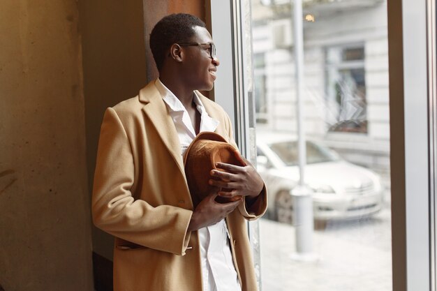 Black man in a brown coat standing by the window