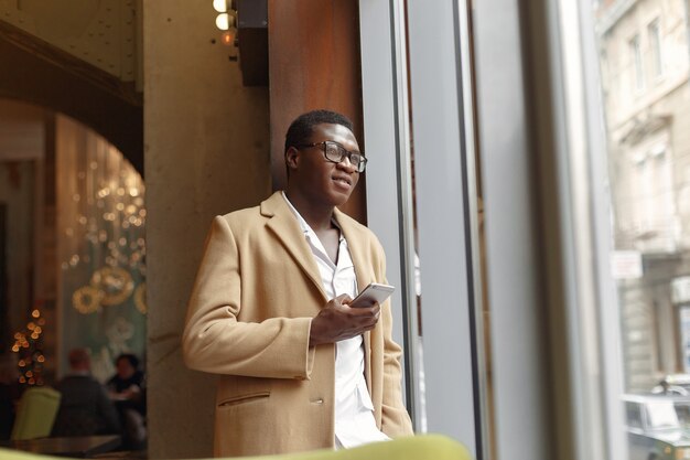 Black man in a brown coat standing with mobile phone