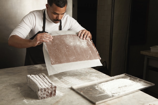 Black man chief preparing freshly baked chocolate cake for packaging, artisan cooking process in confectionery