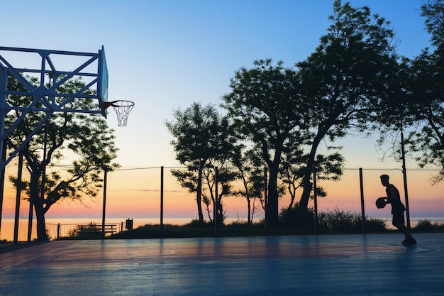 Black man doing sports, playing basketball on sunrise, silhouette