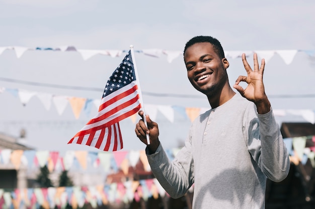 Black man holding American flag and looking at camera with gesture OK