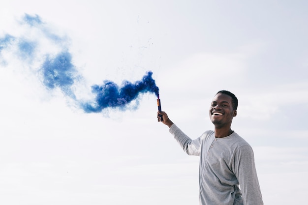 Foto gratuita uomo nero che tiene fumogeni blu