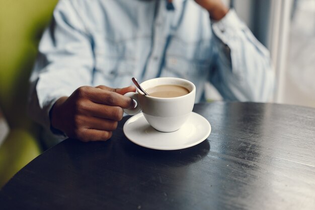 Черный человек сидит в кафе и пьет кофе