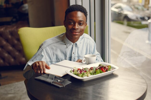 Black man sitting in a cafe and eating a vegetable salad