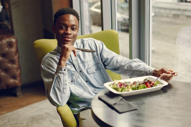 Черный человек сидит в кафе и ест овощной салат